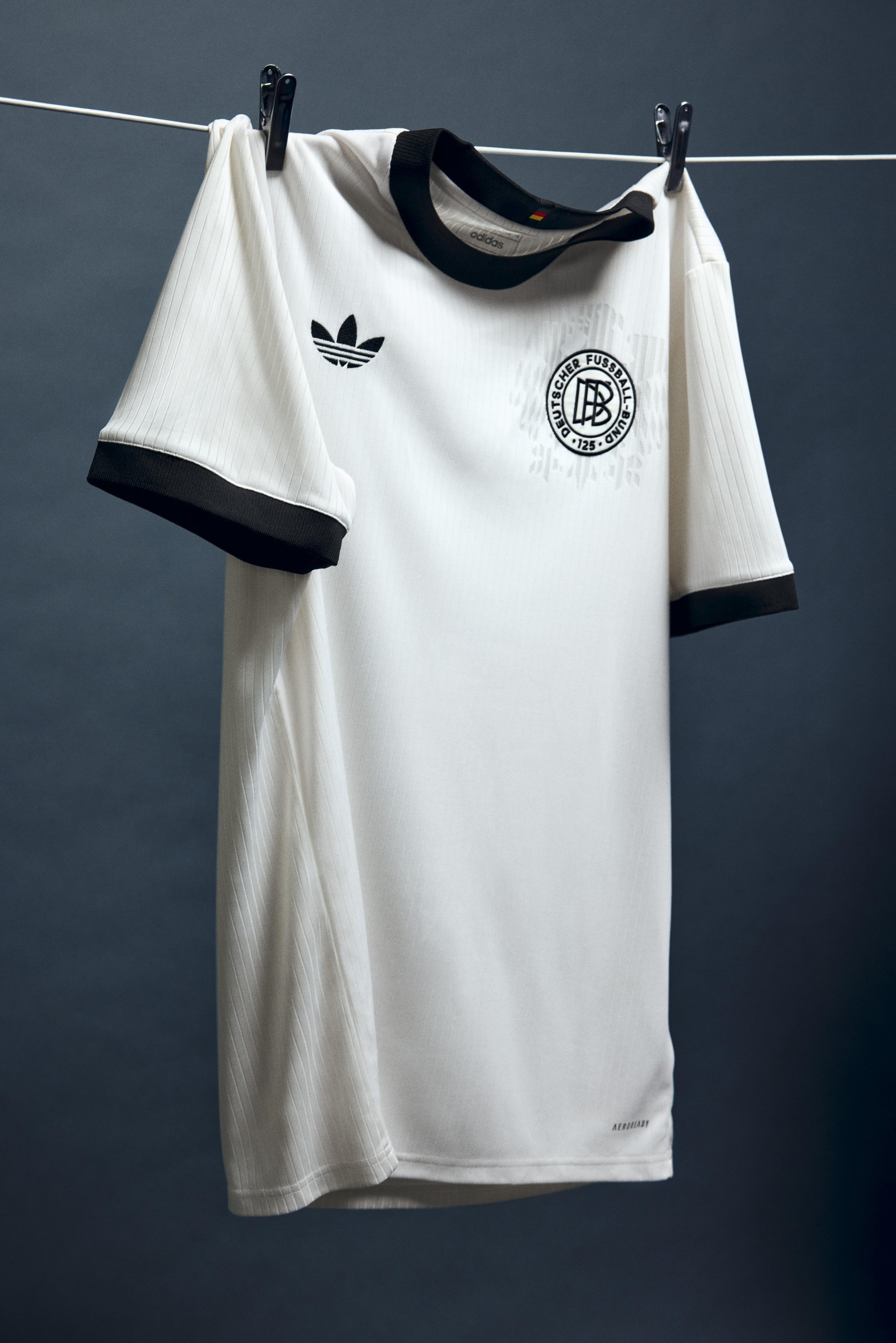 White football jersey hanging on a clothesline, featuring black collar and sleeves, with the Adidas logo and a circular team emblem.