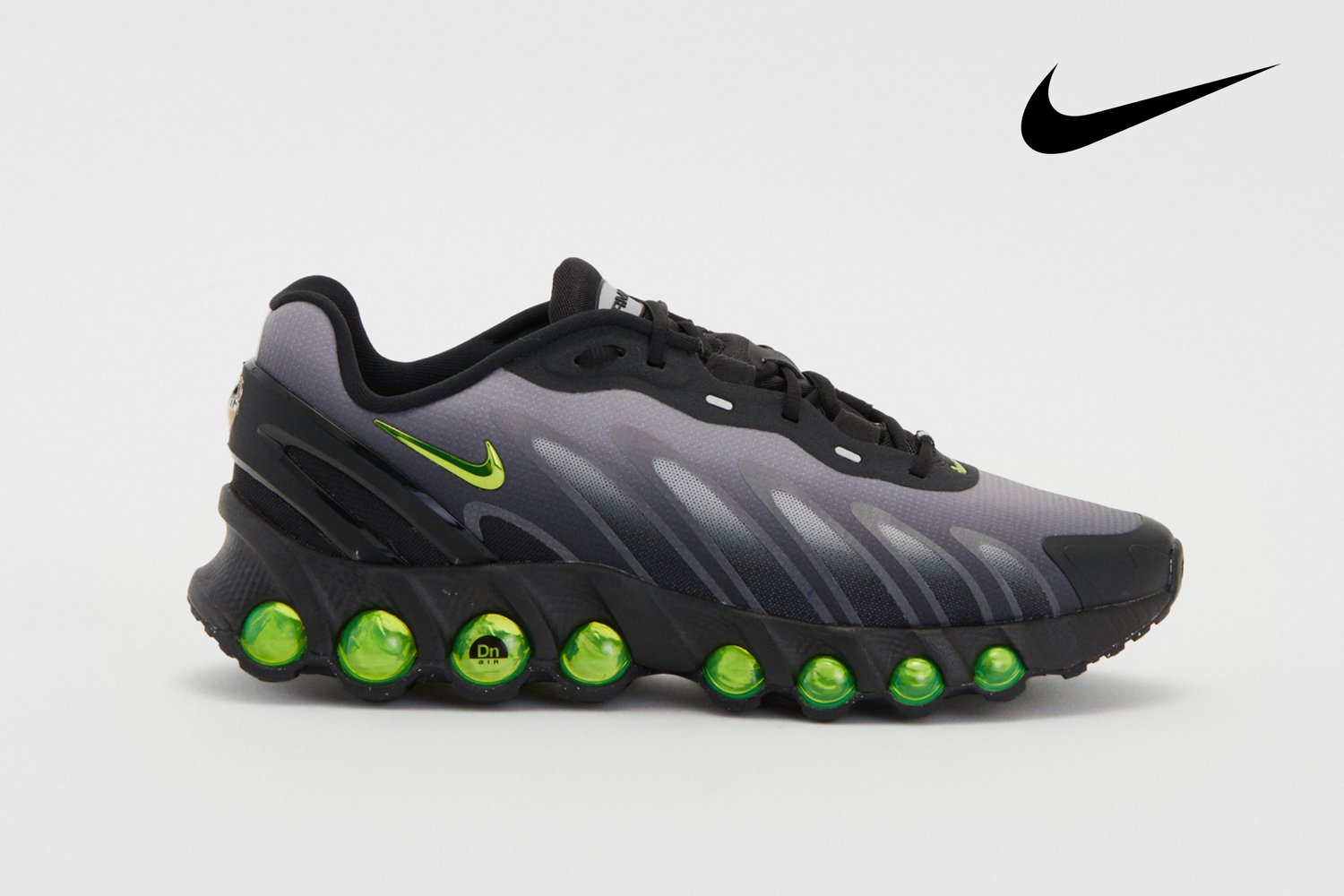 Grijze en zwarte Nike sneaker met een kenmerkende groene zool, opvallend swoosh-logo en een gestructureerd bovenwerk.