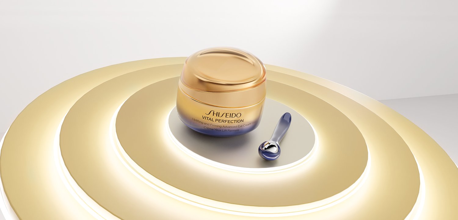 Shiseido Vital Perfection Cremegefäss mit Applikator auf reflektierender Oberfläche, umgeben von konzentrischen goldenen Ringen.