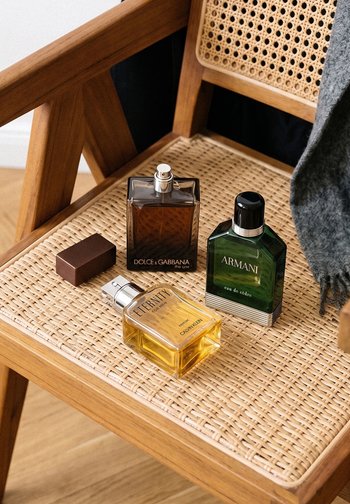 Tres botellas de colonia etiquetadas como Dolce & Gabbana, Armani y Calvin Klein colocadas sobre el asiento de una silla de madera con asiento trenzado de caña.
