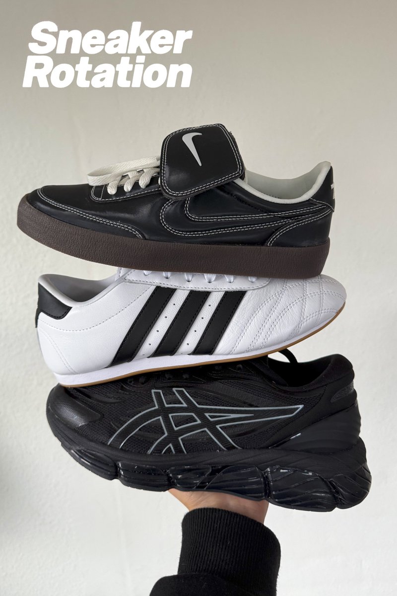 A hand holds three stacked sneakers: black Nike with strap, white Adidas with black stripes, and black Asics with reflective details.