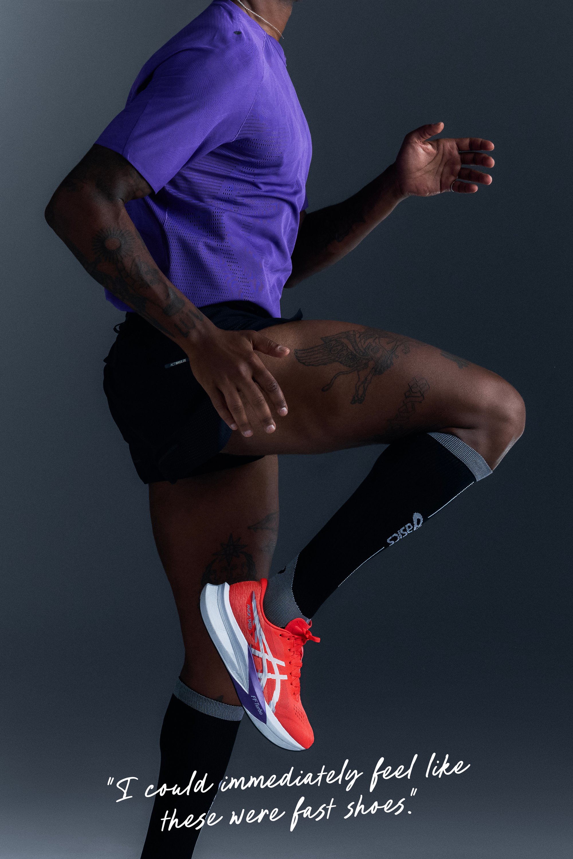 Läufer trägt ein lila Shirt, schwarze Shorts und schwarze Socken, hebt das Bein und präsentiert einen leuchtend roten und weißen Asics Laufschuh.