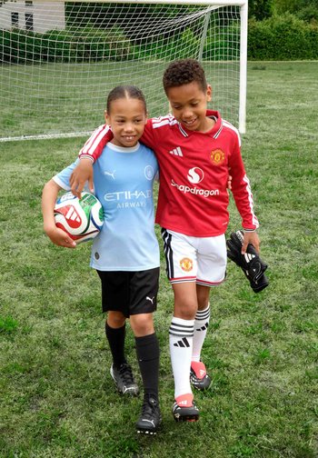 Deux enfants en tenues de football marchent bras dessus bras dessous sur l'herbe près d'un but, l'un tenant un ballon, l'autre des gants de gardien.