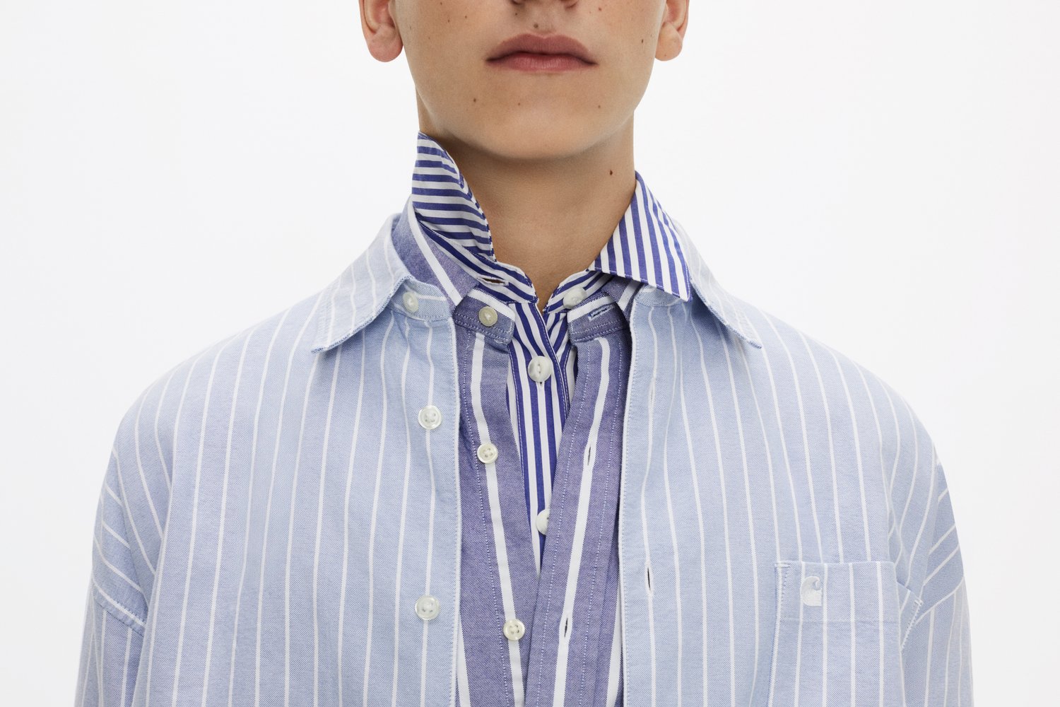 A young person wears a layered shirt with blue and white stripes, featuring a large collar and buttons visible down the front.