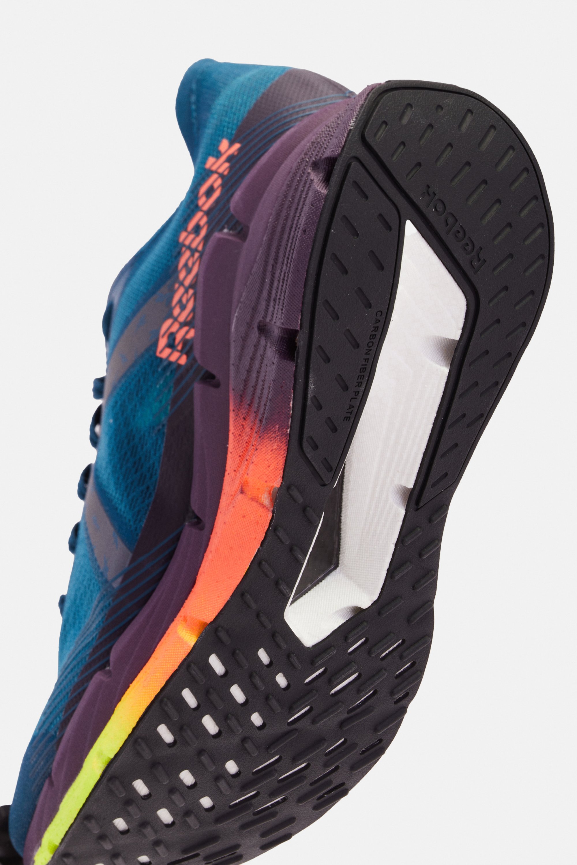 Una vista en primer plano de la parte inferior de una zapatilla de running Reebok en azul y morado, destacando su suela texturizada y un degradado de colores brillantes.