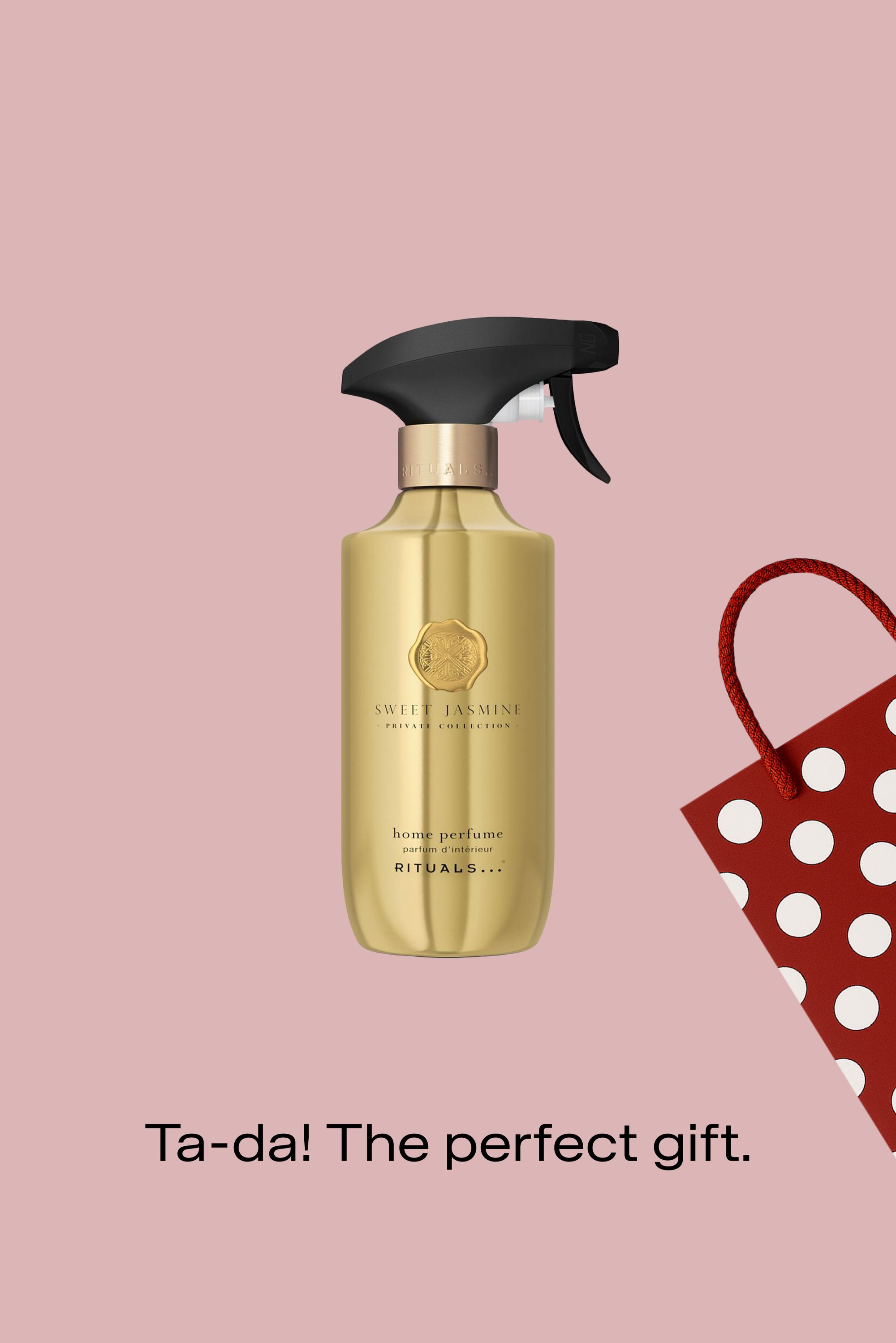 Spruzzatore in metallo dorato etichettato "Sweet Jasmine", con un ugello nero, accanto a una borsa regalo rossa con pois bianchi su uno sfondo rosa.
