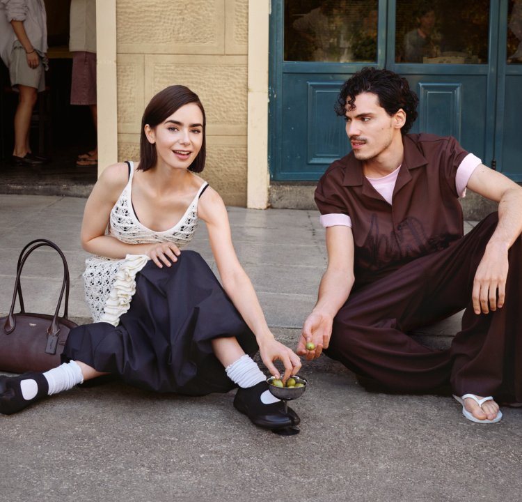 Jeune femme et homme assis sur un trottoir, partageant des olives vertes dans un bol devant un bâtiment aux portes bleues.