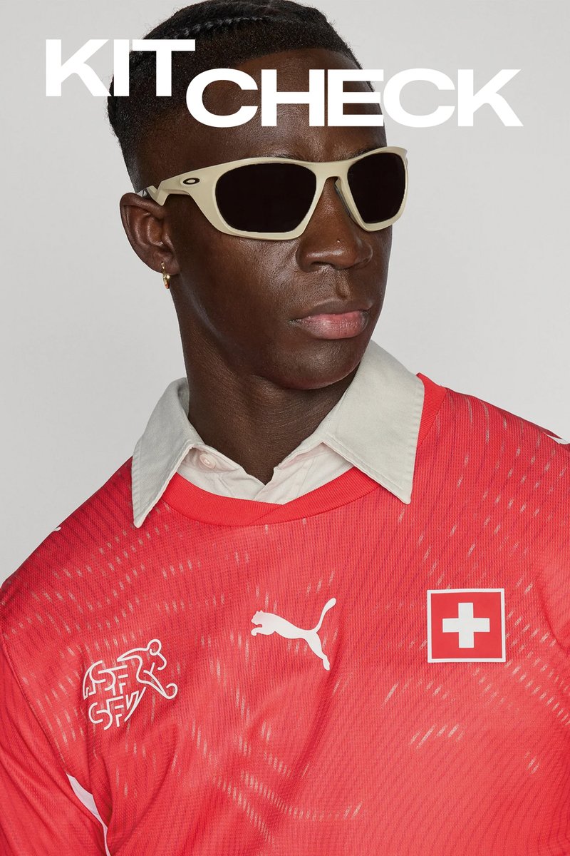 Homme portant des lunettes de soleil beiges, un maillot de football suisse rouge avec le logo Puma et une chemise blanche à col en dessous, légèrement tourné vers la droite.