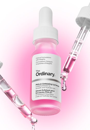 Bouteille en verre rose avec pipette blanche, étiquetée "Sérum Exfoliant pour les Lèvres PHA 5%". Un liquide clair et visqueux s'écoule de la pipette.