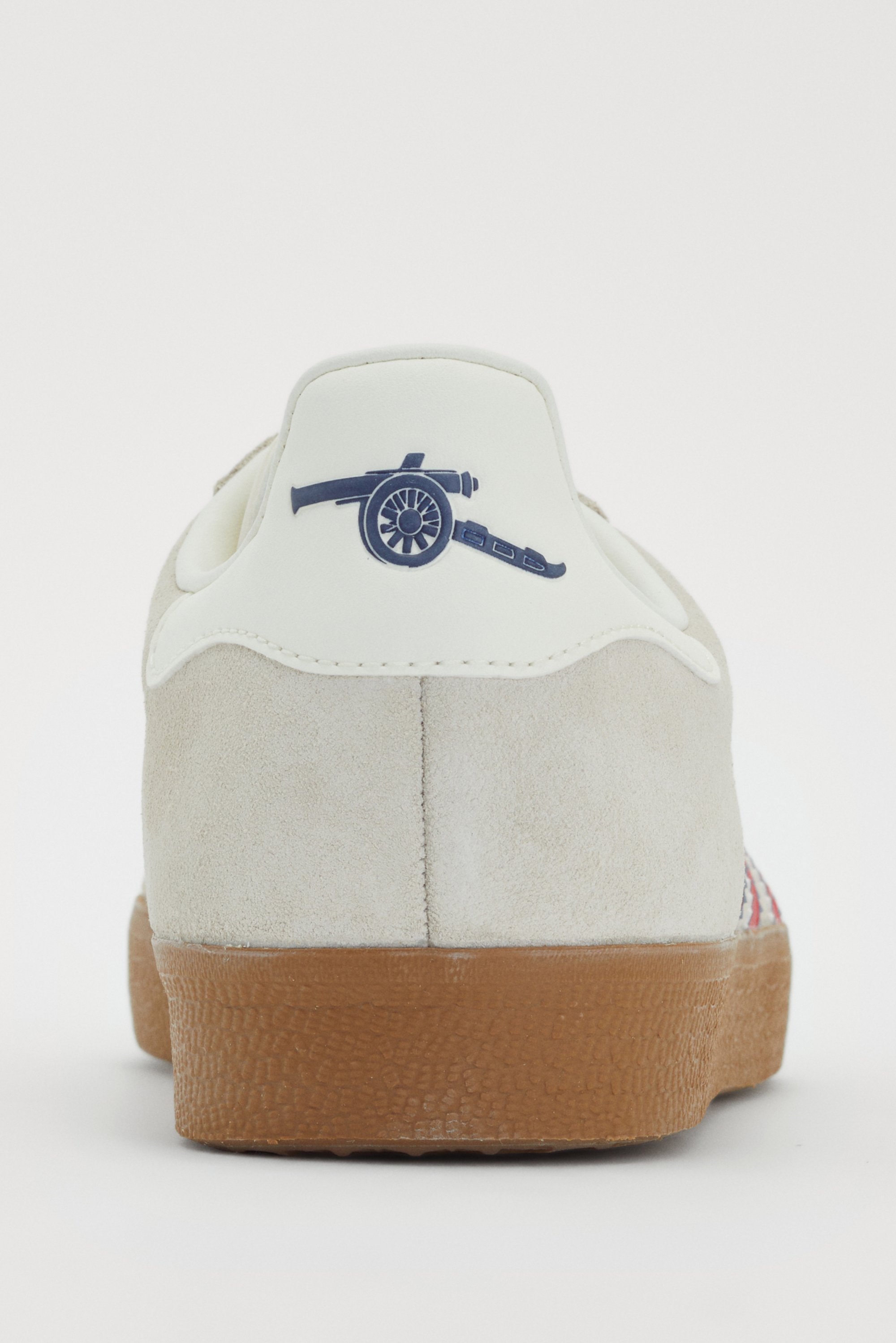 Grijze suède sneaker met een witte hieltab, versierd met een blauw kanonlogo, geplaatst tegen een plain witte achtergrond.