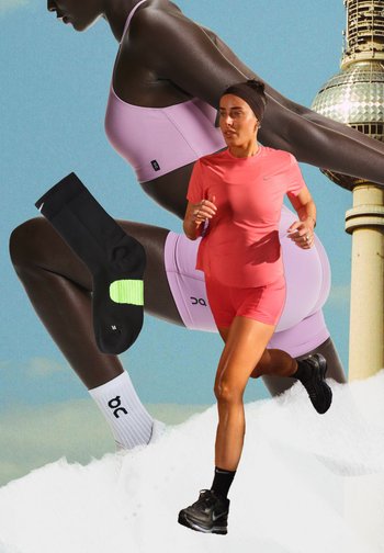 Kvinde løber i koralfarvet træningstøj og sorte sko, med en større baggrund af en anden kvinde, der strækker ud i lilla sportstøj og en sort sok, der flyder i nærheden.