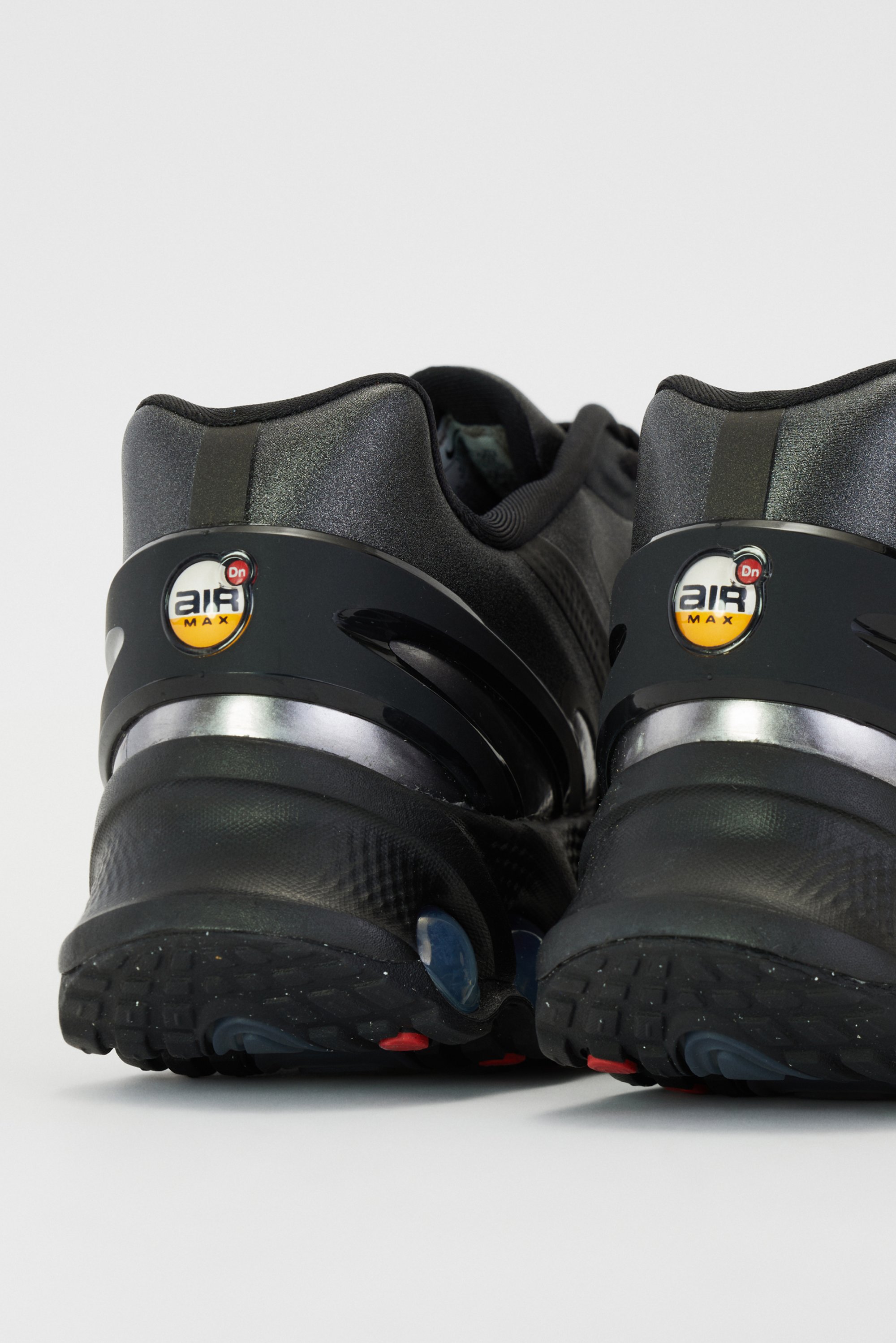 Zwarte hardloopschoenen met een slank ontwerp, uitgerust met een zichtbare luchtkusseneenheid en een logo op de hak. Achtergrond in neutrale kleur.
