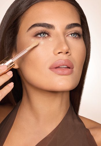 Kvinde, der påfører flydende concealer under øjet med en applikator i blød spids, fremhæver fejlfri hud og naturlig makeup.
