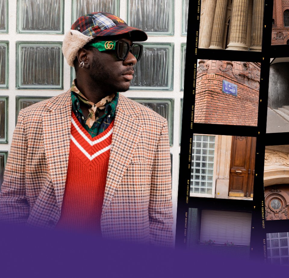 Ein Mann mit Sonnenbrille und modischer Kleidung posiert vor einer strukturierten Glaswand und präsentiert mutige Muster und Farben in seinem Outfit.