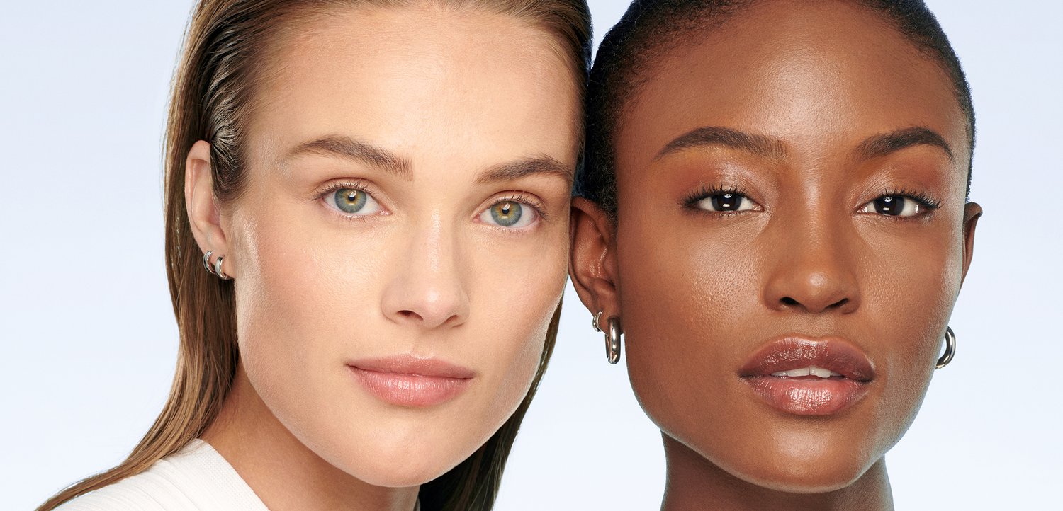 Due donne con pelle chiara e trucco naturale affrontano frontalmente uno sfondo chiaro e semplice, mettendo in risalto la diversità di bellezza e tonalità della pelle.