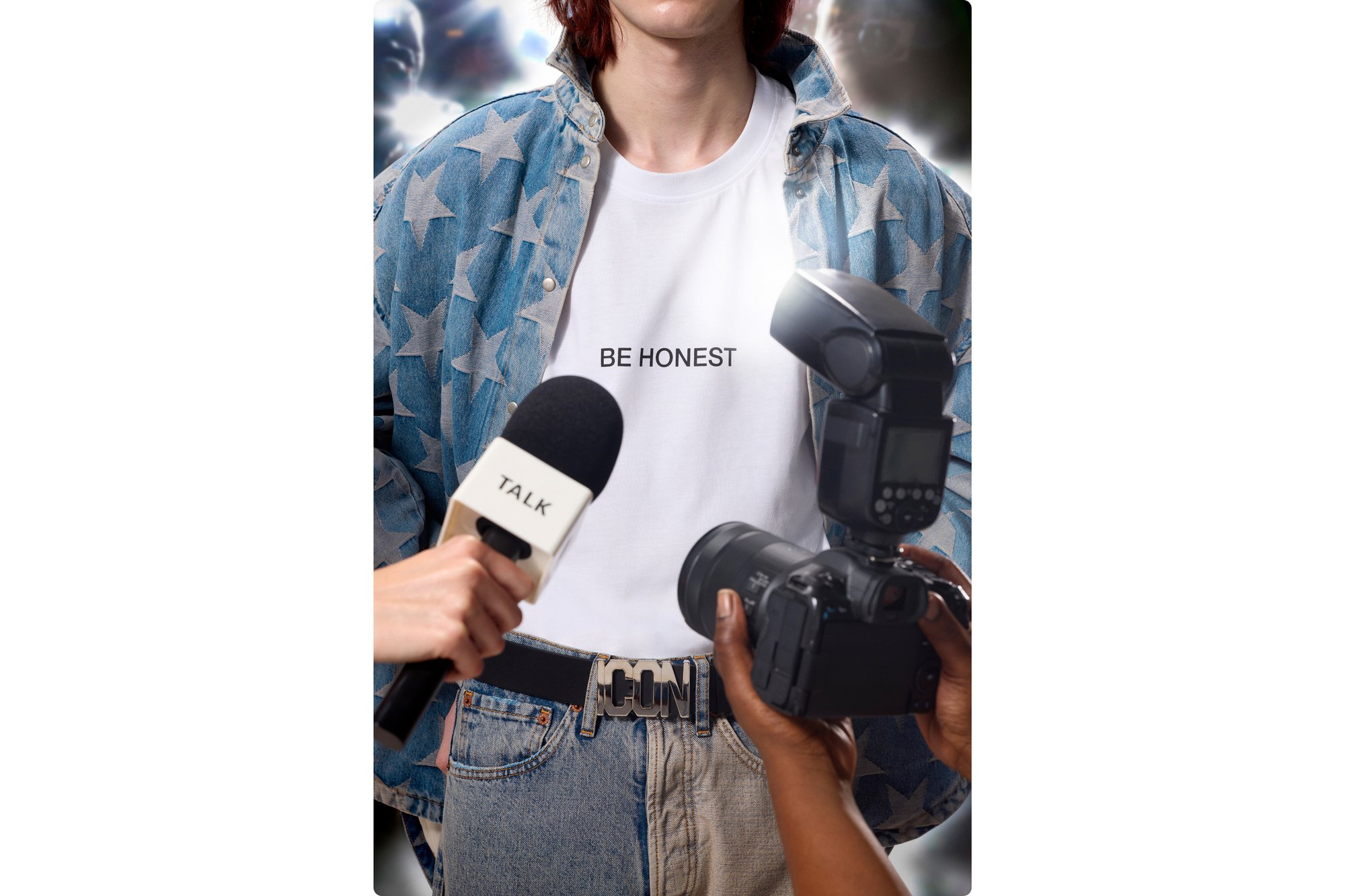 Una persona che indossa una giacca con motivo a stelle e una maglietta con scritto 'ESSERE ONESTI' viene intervistata, con un microfono e una telecamera in vista.