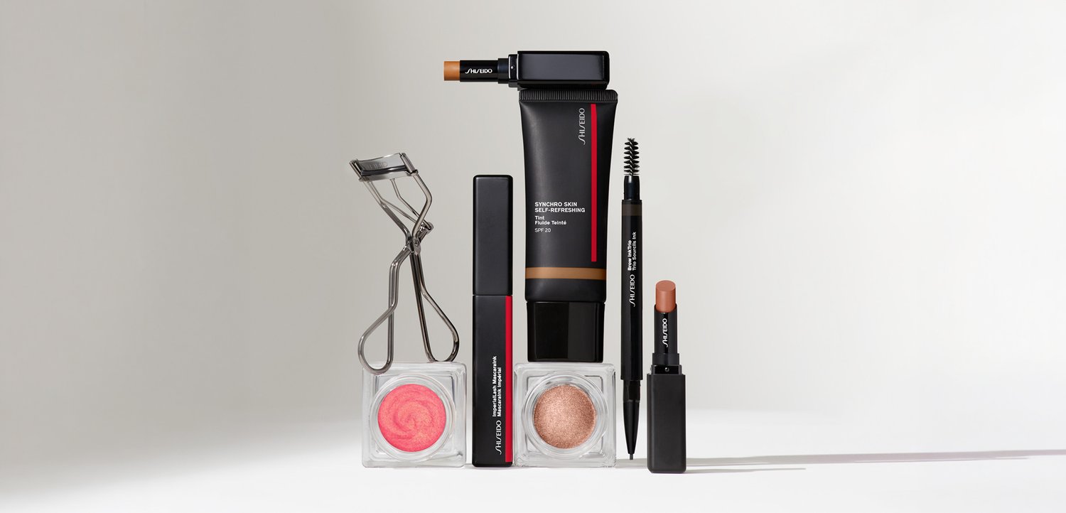 Wimpernzange, rosa und bronzefarbener Creme-Make-up, schwarze Mascara, Foundation-Tube, Augenbrauenstift und Nude-Lippenstift auf weißem Hintergrund angeordnet.