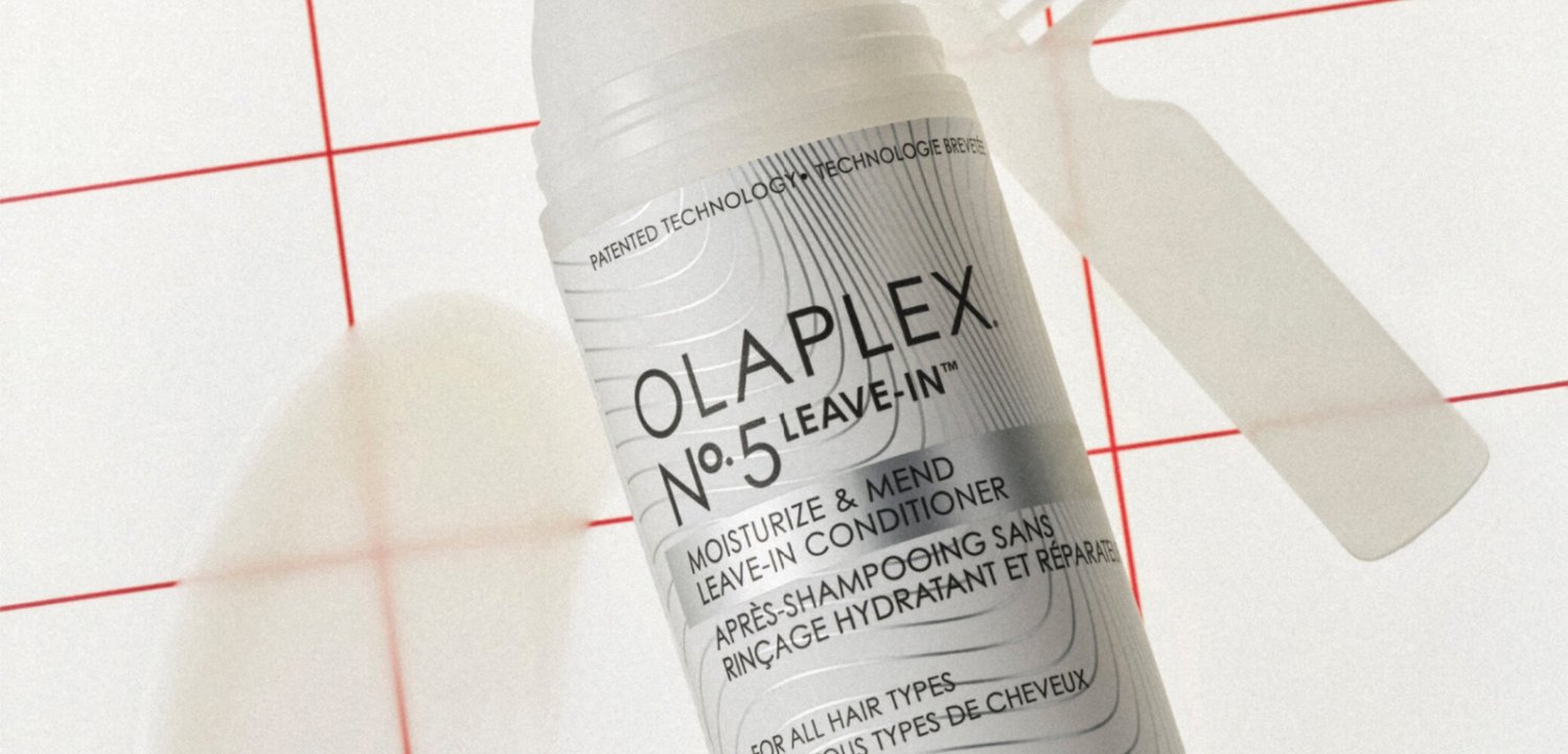 Olaplex No. 5 Leave-In Conditioner bottle on white surface with red grid lines, shadow of a hand and a comb nearby.