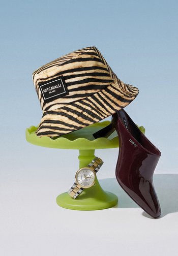 Csíkos Just Cavalli bucket kalap, bordó patent DKNY mule cipő és kéttónusú karóra zöld talapzaton kék háttér előtt.
