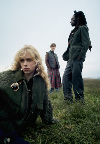 Trei persoane în modă outdoor: o jachetă verde cu matlasare, o fustă în carouri și pantaloni textură. Cadru natural cu culori discrete.