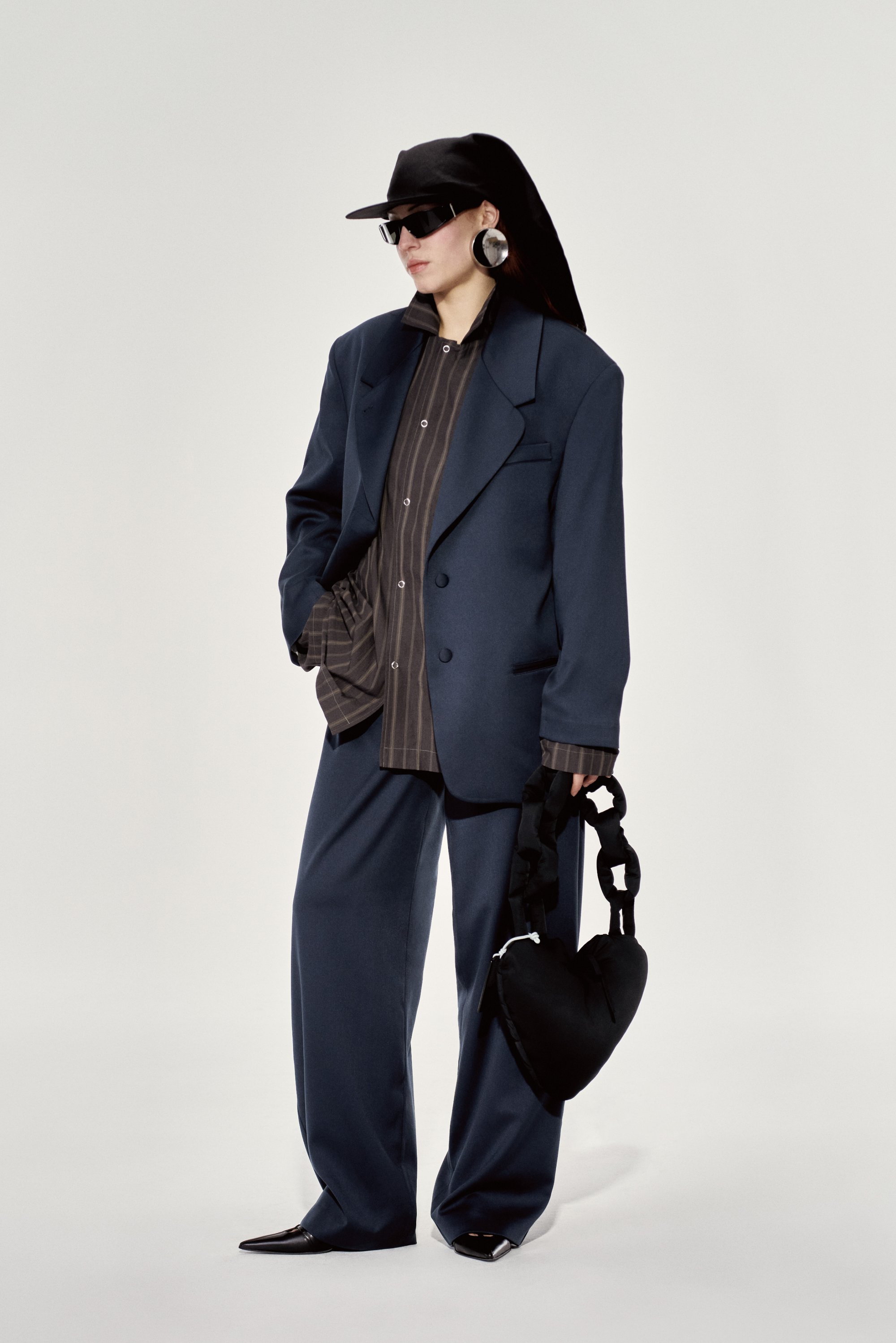Blazer de gran tamaño en color navy sobre una camisa de rayas, pantalones de pierna ancha, sombrero negro, gafas de sol y un bolso negro en forma de corazón.