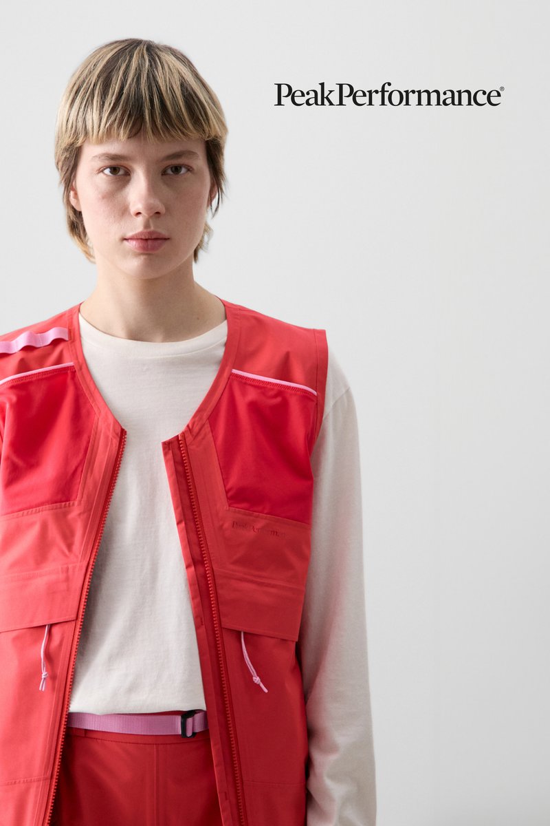 A person with short, light-colored hair wears a bright red vest over a white shirt, standing against a neutral background, featuring the PeakPerformance logo.