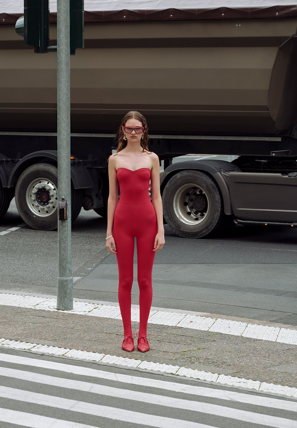 Rouge, sans bretelles, avec un décolleté en forme de cœur, associé à des lunettes de soleil rouges, se tenant sur un passage piéton près d'un camion.