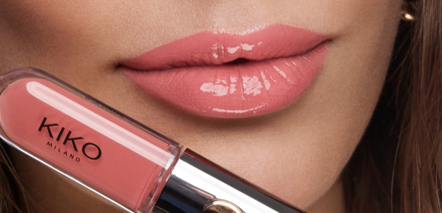 Labios rosas brillantes junto a un tubo de brillo de labios rosa de KIKO Milano sostenido cerca del rostro.