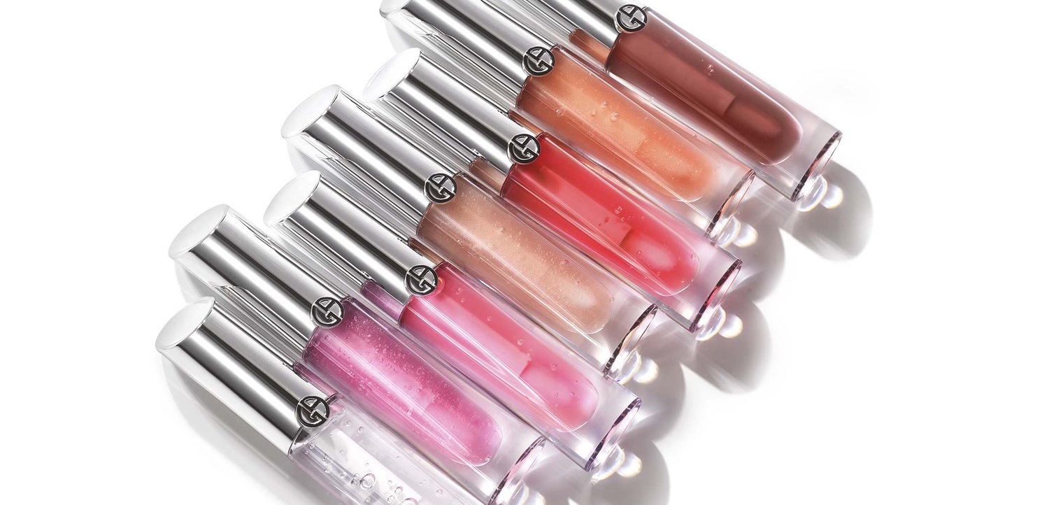 Un ensemble de huit tubes de gloss à lèvres transparents avec des caps en argent. Les couleurs varient du clair au rose, avec différentes finitions scintillantes.