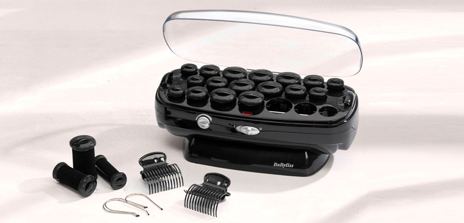 Zwart elektrisch haarrollerset met 20 rollers, beschermend doorzichtig deksel, twee zwarte haarclips en twee metalen haarspeldclips op een witte ondergrond.