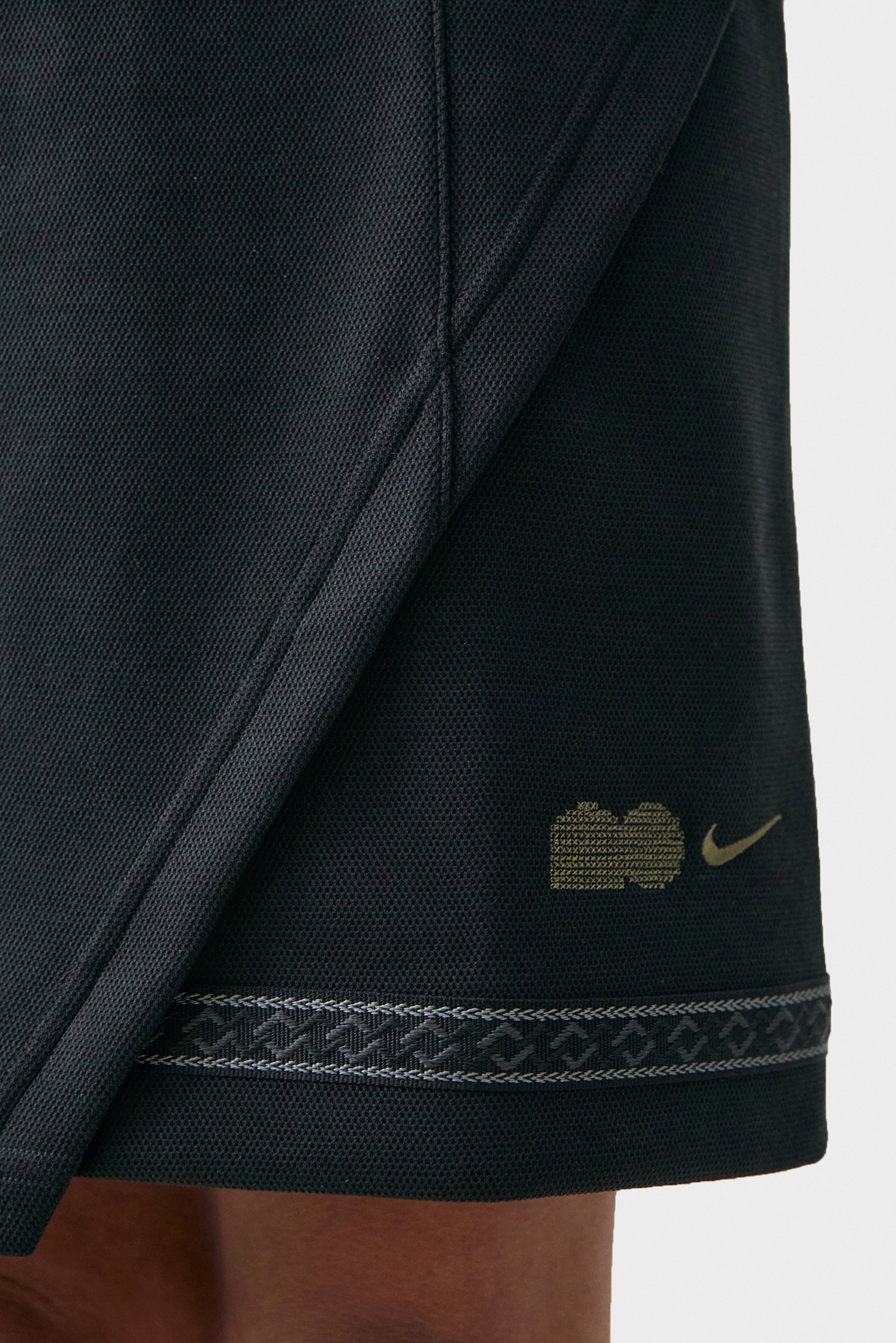 Pantalones cortos deportivos negros con un tejido texturizado, que presentan un logo dorado y un ribete decorativo plateado en el dobladillo. Enfocado en el diseño de ropa deportiva.