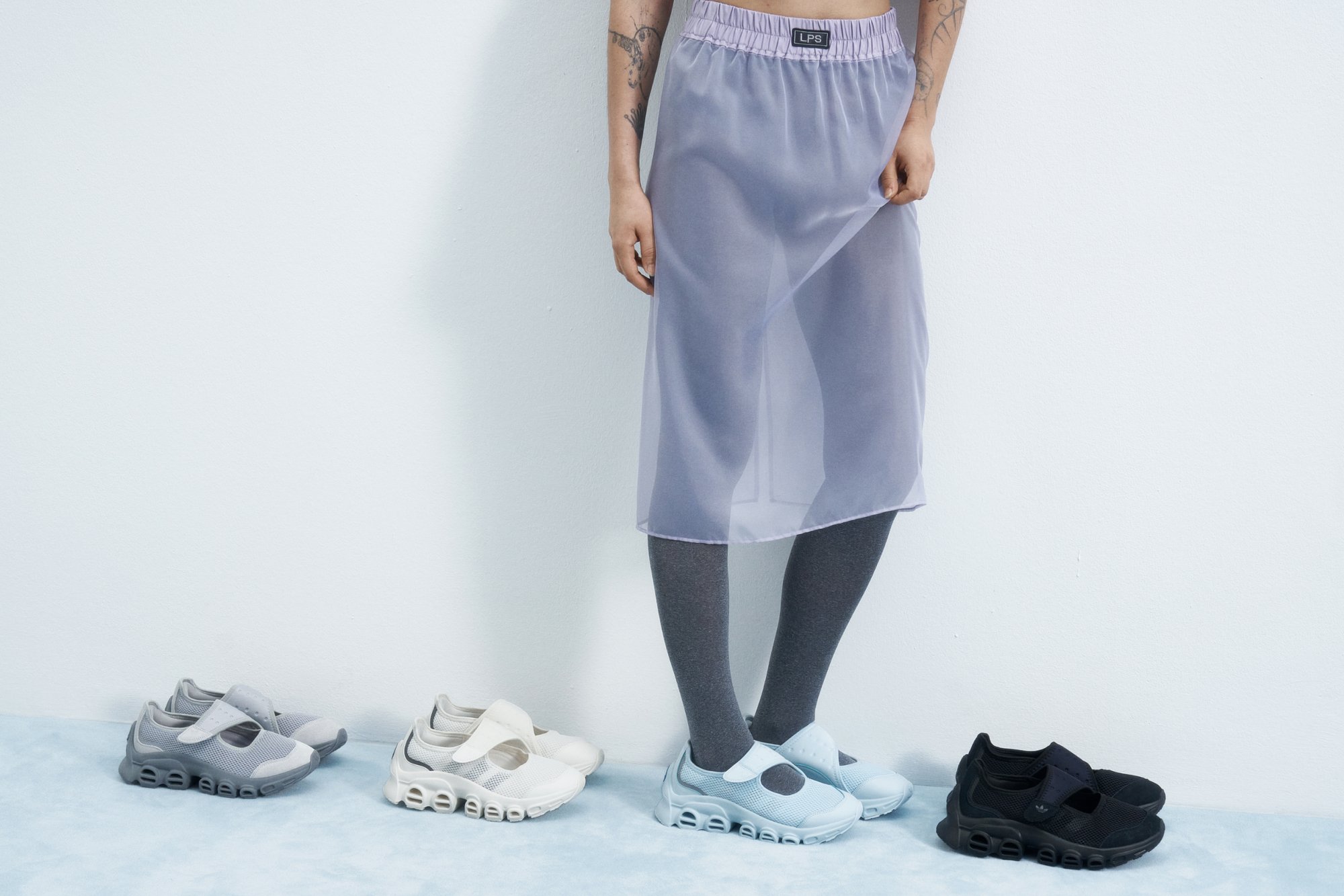 Falda midi de lavanda translúcida con cintura elástica, combinada con calcetines grises y zapatillas en variaciones de gris, blanco, negro y azul.