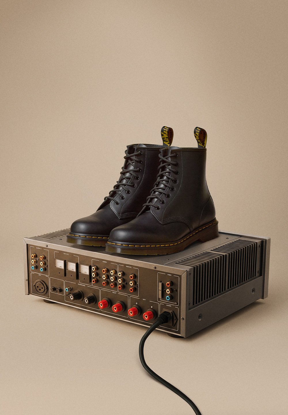 Sorte lær ankle boots med rund tå, snøremønster og gul søm, vist på en sølvfarget lydutstyrsenhet.