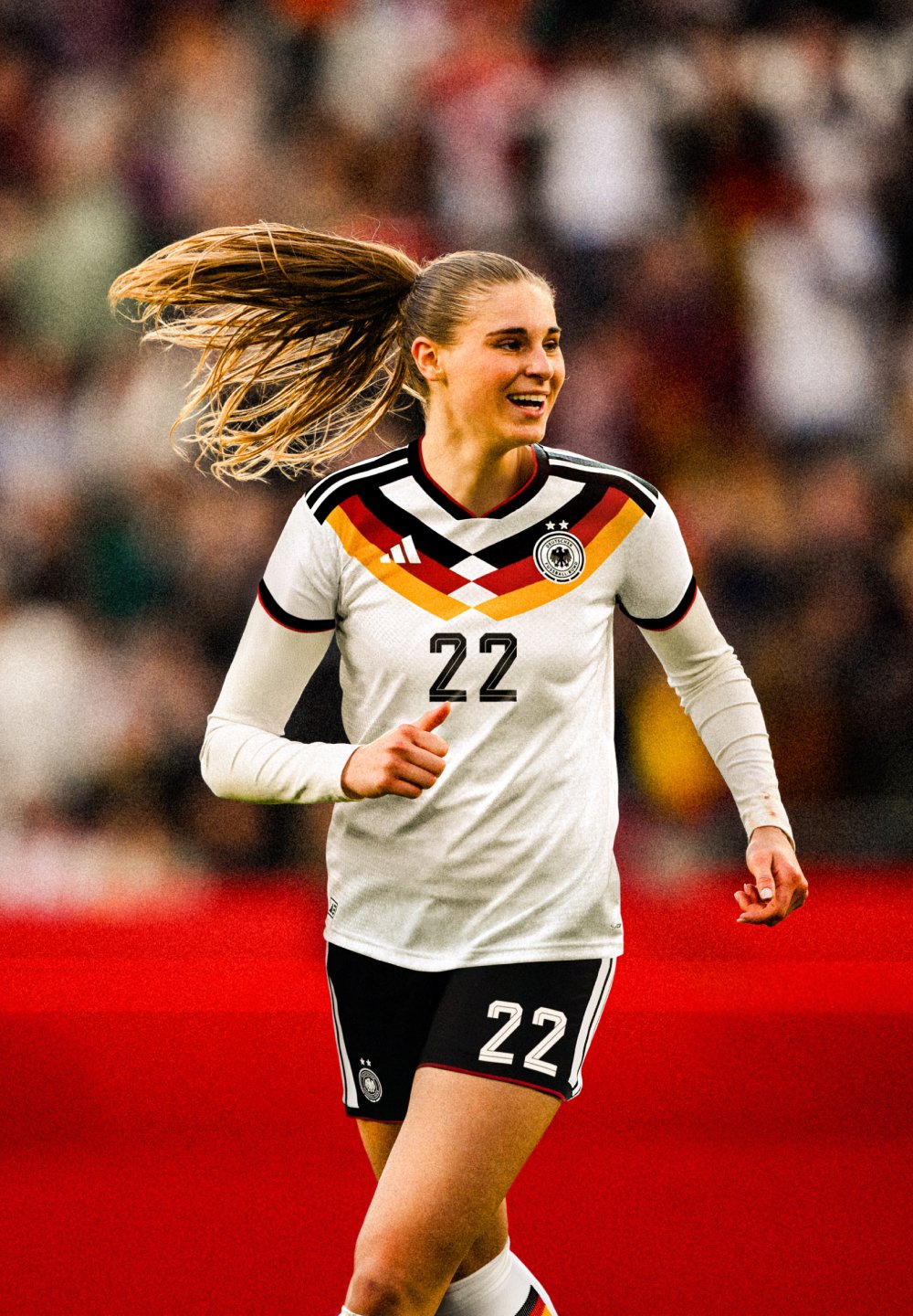 Kobiłka piłkarka w niemieckim białym i czarnym stroju z numerem 22, biegnąca i uśmiechająca się na boisku, z rozmytym tłem tłumu.
