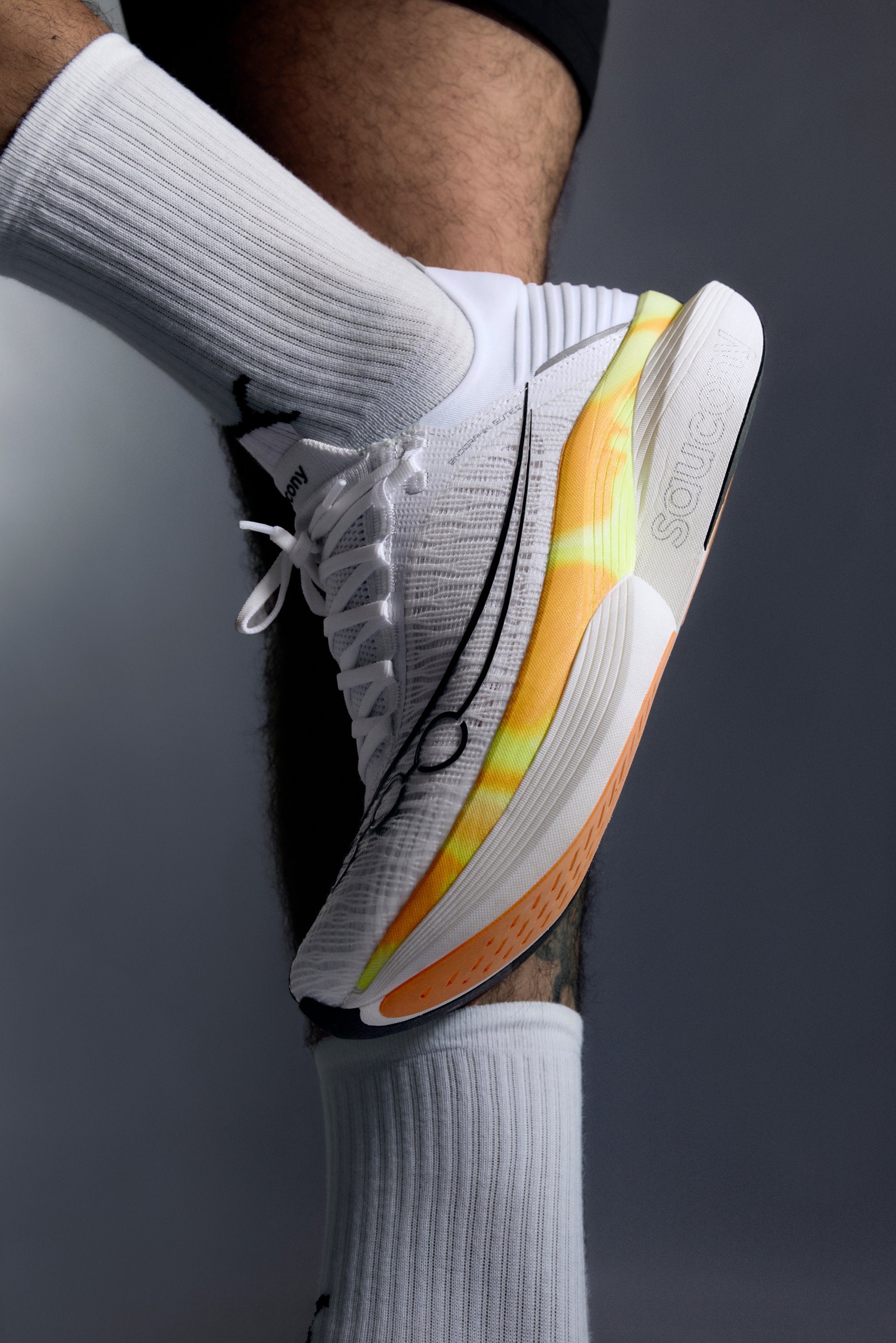 Balti bėgimo bateliai su tekstūruotu paviršiumi, ryškiai geltonais ir oranžiniais akcentais ant pado, bei juodais akcentais. Derinami su tekstūruotomis baltomis kojinėmis.