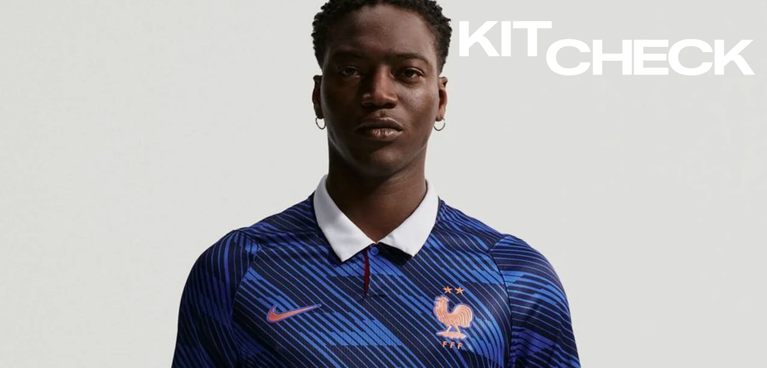 Mann trägt ein blaues Trikot der französischen Fussballnationalmannschaft mit Nike-Logo und zwei Sternen über dem Hahn-Emblem, stehend vor einem schlichten hellen Hintergrund.