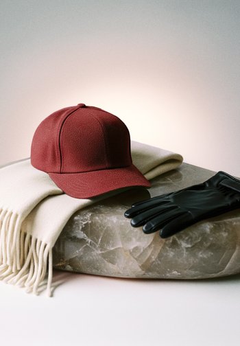 Punane pesapallimüts kreemja salliga ja mustad nahkkindad, mis puhkavad ümaral kivipinnal.