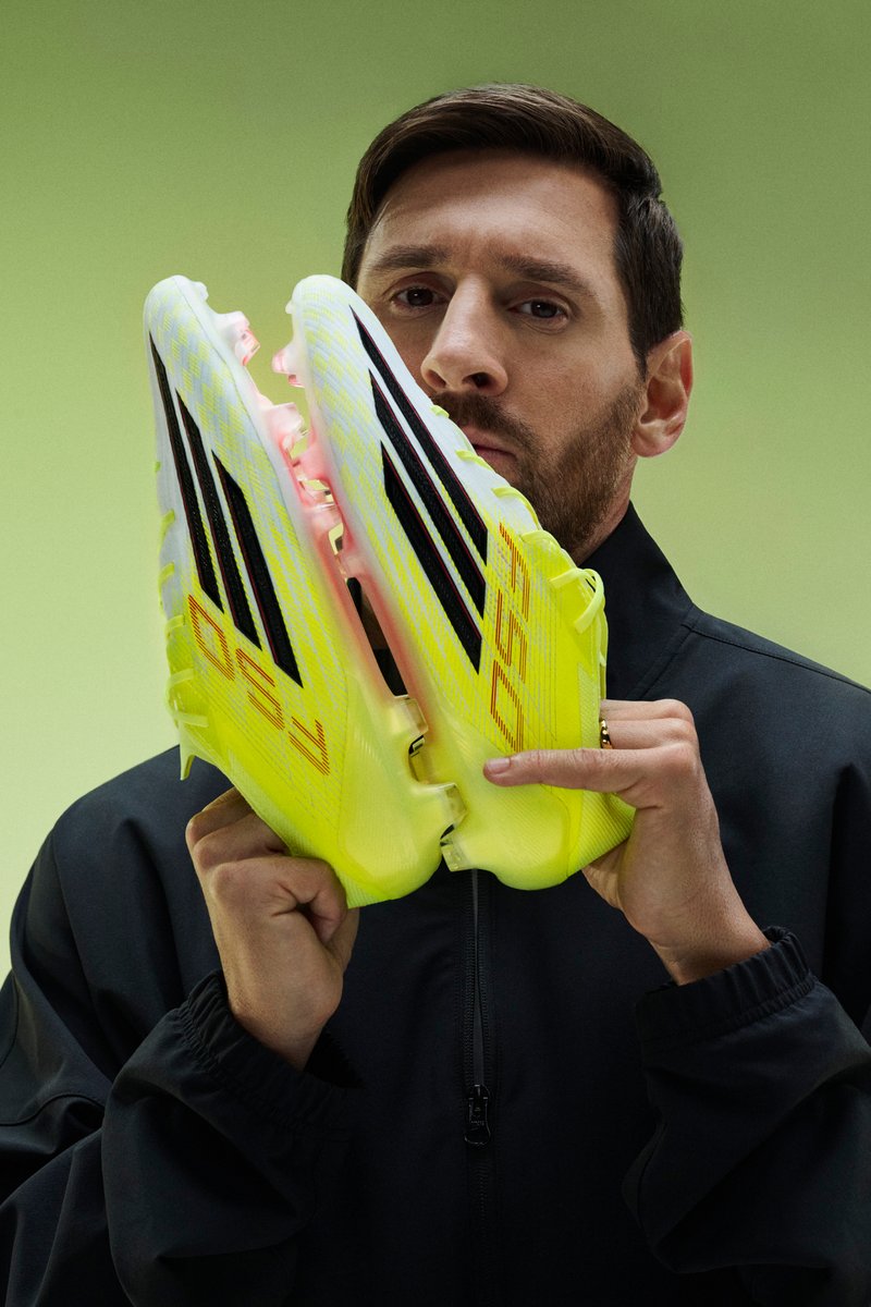 Man holding a pair of bright yellow soccer cleats with black stripes close to his face against a green background.