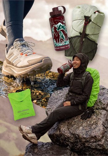 Wanderer in schwarzer Regenkleidung sitzt auf einem Felsen, trinkt aus einer Wasserflasche, mit grünem Rucksacküberzug, wasserdichten Schuhen und separat gezeigter Wanderausrüstung.