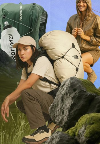 Deux randonneurs avec de grands sacs à dos, l'un accroupi avec une bouteille d'eau, l'autre souriant dans une veste à capuche au milieu de rochers couverts de mousse.