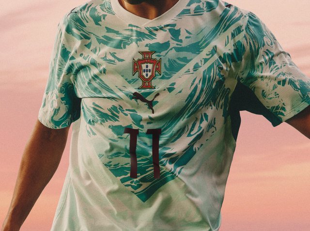 Maglia nazionale di calcio del Portogallo con motivi astratti verdi, logo Puma, stemma della squadra e numero 11 sul torso di un giocatore su sfondo rosa.