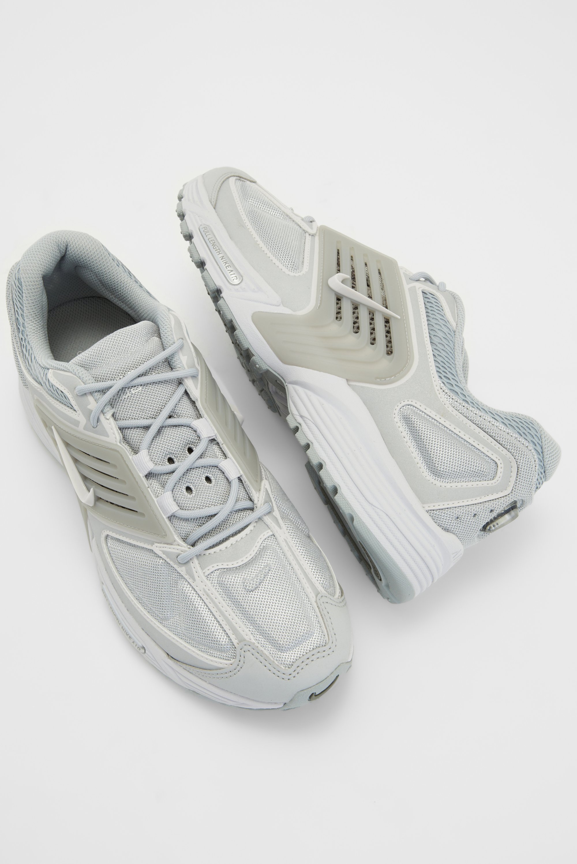 Grijze sportieve schoenen met gaasdetails en subtiele witte accenten, gepositioneerd tegen een effen witte achtergrond.
