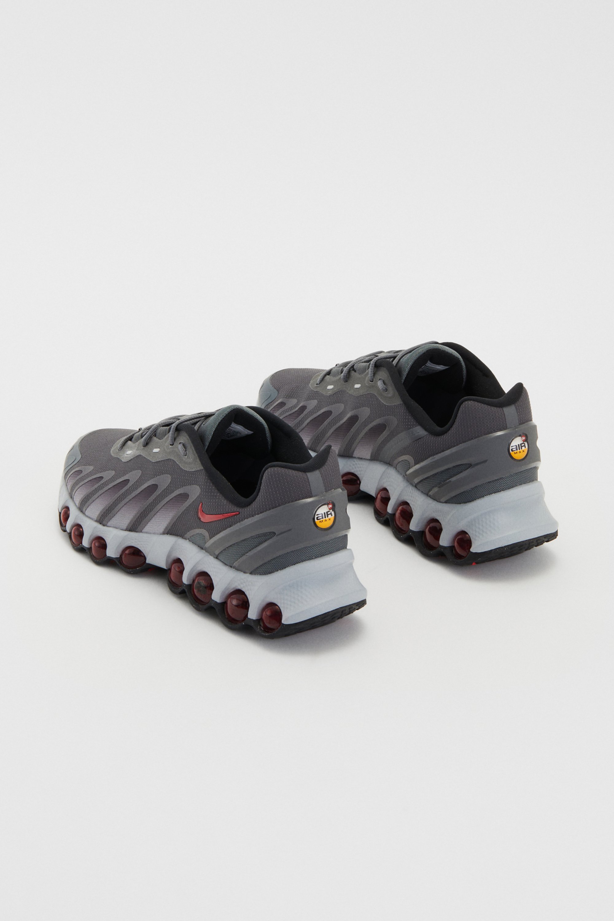 Grijze Nike sneakers met een onderscheidende zoolvoorziening van rode dempingspods, getoond vanuit een hoekige kijk tegen een witte achtergrond.