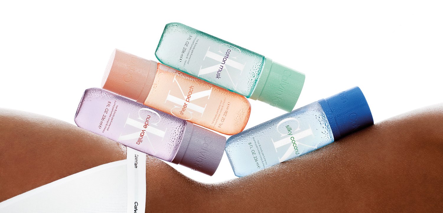 Vier kleine kleurrijke bodymist-flesjes met de labels cotton musk, sheer peach, nude vanilla en silky coconut die rusten op de rug van een donkerhuidig persoon.