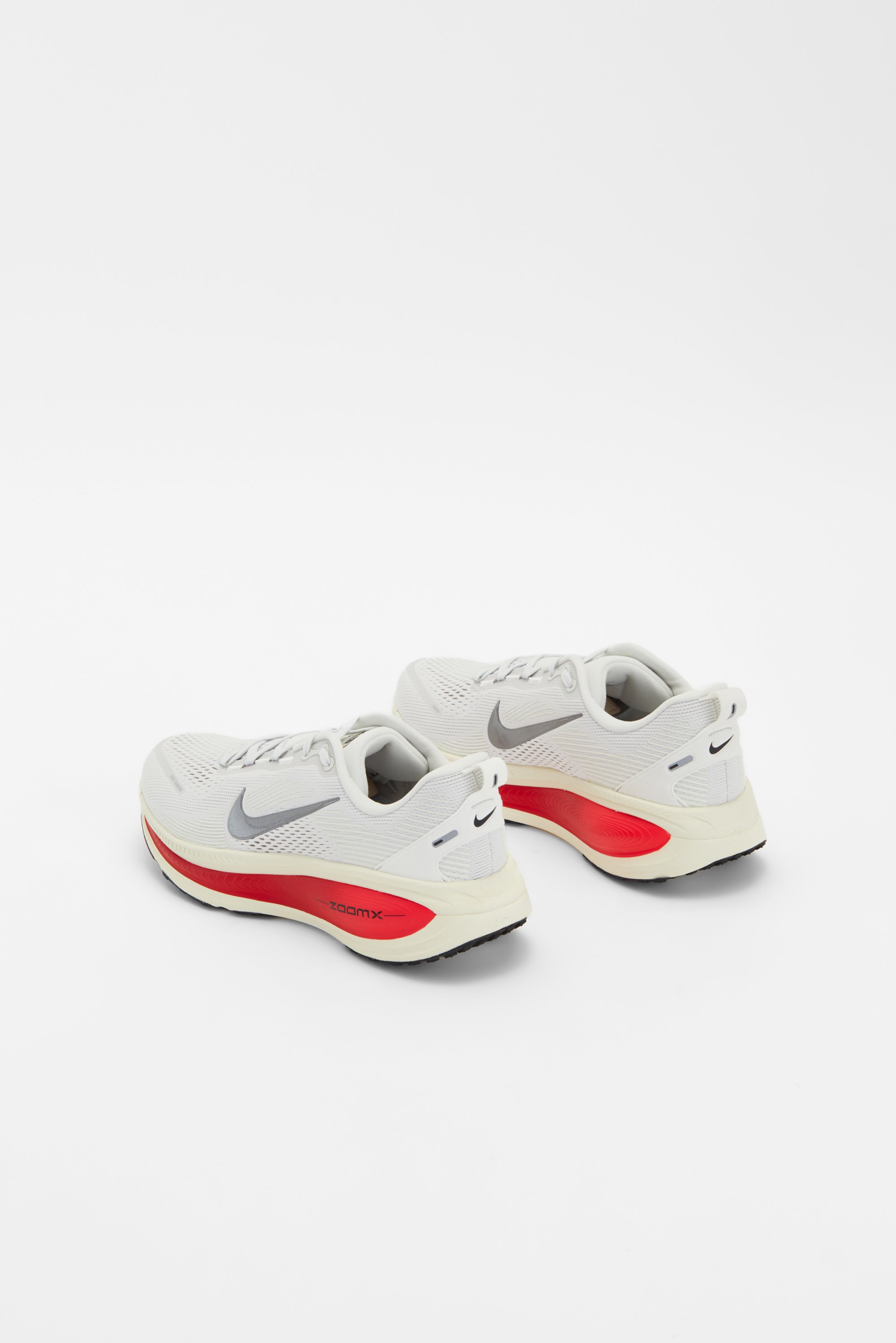 Zapatillas de correr Nike en blanco y gris con un acento rojo, mostradas desde la parte trasera sobre un fondo plano. Presentan un diseño de malla transpirable.