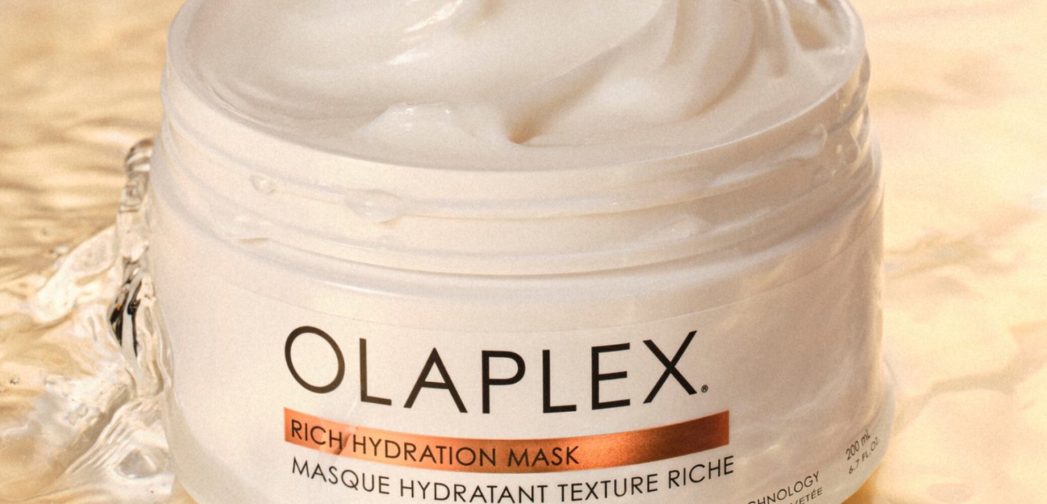 Potje Olaplex Rich Hydration Mask met witte crème erin, geplaatst op een nat oppervlak met waterdruppels eromheen.