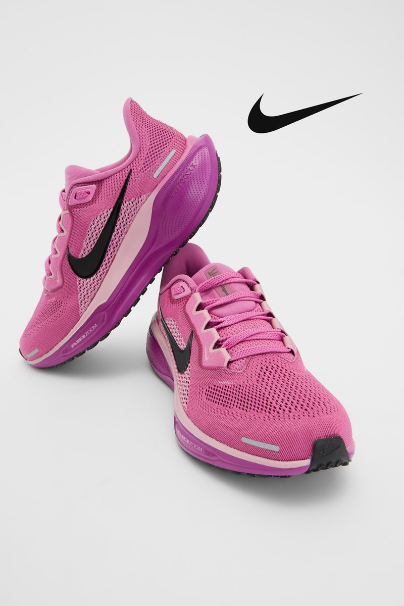 Pink Nike athletic shoes with black swoosh logo, displayed at an angle on a white background, showcasing mesh upper and cushioned sole.