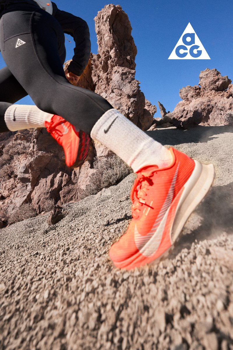 Corridore che indossa sneakers arancioni vivaci, calzini bianchi Nike e leggings neri, che corre su un terreno roccioso del deserto sotto un cielo azzurro limpido.