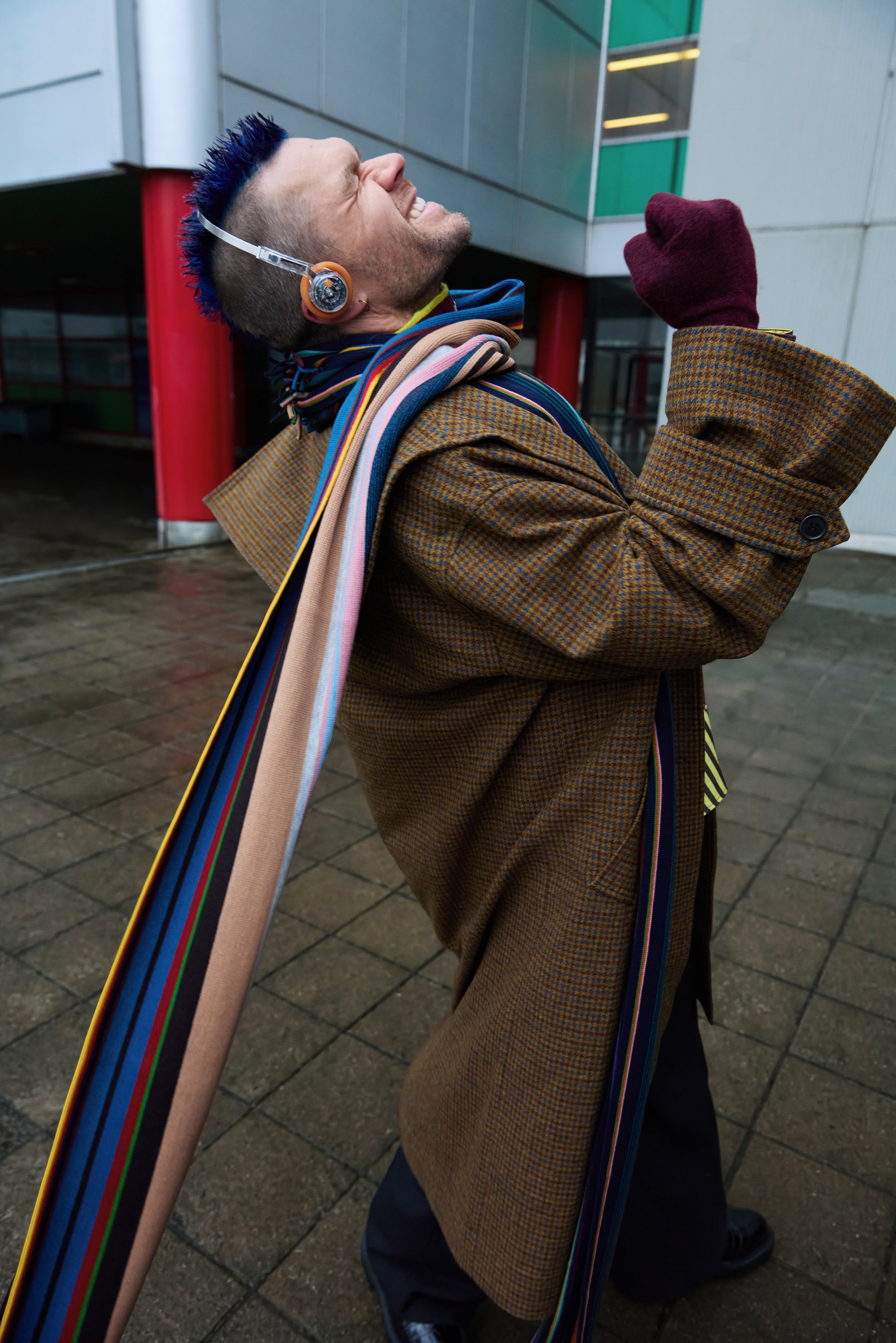 Ruskehtava ruutupintainen ylipuku, jossa on suuret hihat, ja sen päällä kerroksittain monivärisiä raidallisia huiveja. Hahmolla on kuulokkeet ja viininpunaiset käsineet.