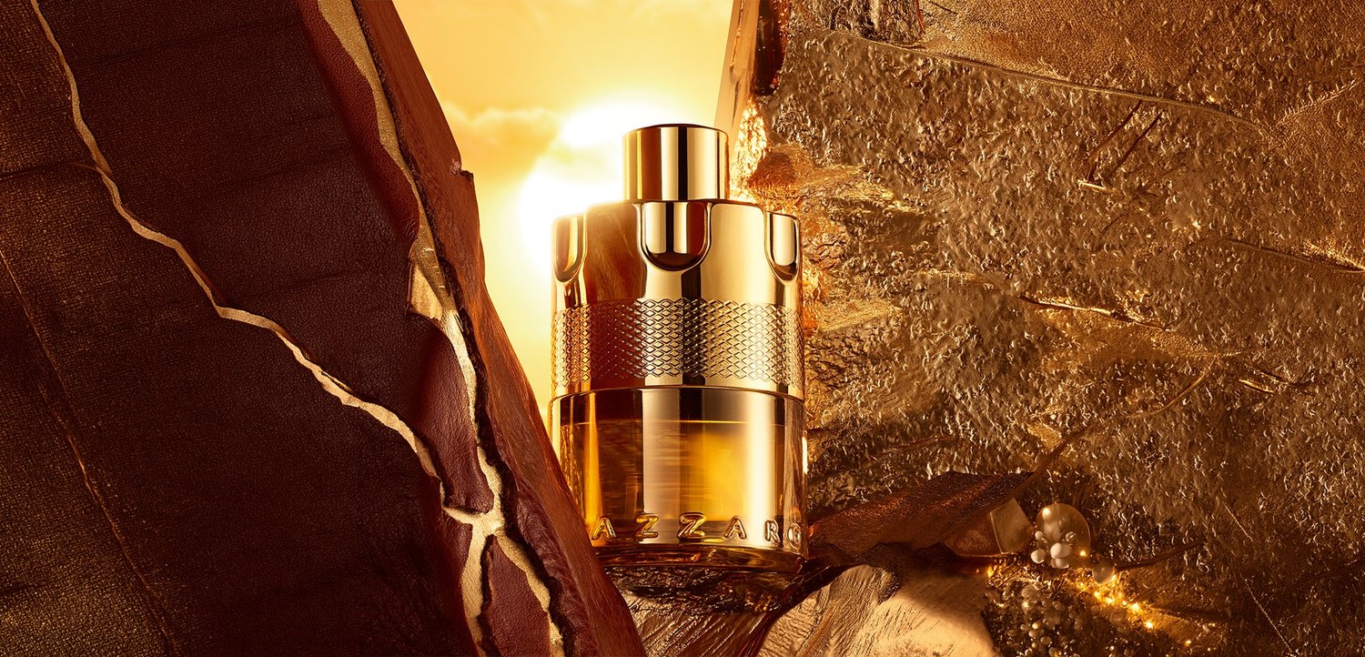 Flacon de parfum ton doré avec un design texturé placé entre des surfaces texturées sombres et dorées, éclairé par une lumière solaire chaude en arrière-plan.